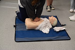 Schüler einer 8. Klassen beim Reanimationstraining an einer auf dem Boden liegenden Puppe